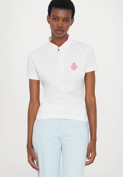 Hvit polo skjorte med en rosa brodert logo, med Mandarin-krage, knappegate og korte ermer, kombinert med lyseblå bukser.