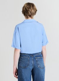 Chemise bleu clair à manches courtes avec col plié ; tissu lisse et coupe décontractée. Associée à un jean en denim bleu taille haute avec poches arrière.