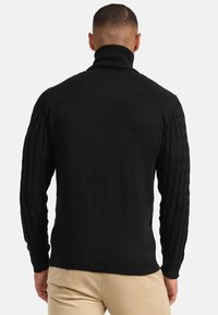 Schwarzer gestrickter Pullover mit hohem Kragen, ausgestattet mit strukturierten Zopfmusterärmeln und einem gerippten Saum sowie Bündchen.