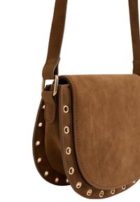 Brūnas zamšādas crossbody soma ar zelta aksesuāriem, kas aprīkota ar apaļām metāla iedobēm pa malām un plakanu, noapaļotu formu.