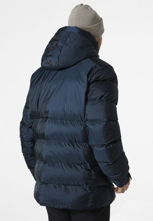 Donkerblauwe pufferjack met capuchon, voorzien van een doorgestikte design en logo-detail op de achterkant, gemaakt van glanzend, lichtgewicht materiaal.