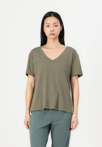 Olive green V-neck t-shirt made of soft fabric with short sleeves and a relaxed fit, paired with light blue green pants.