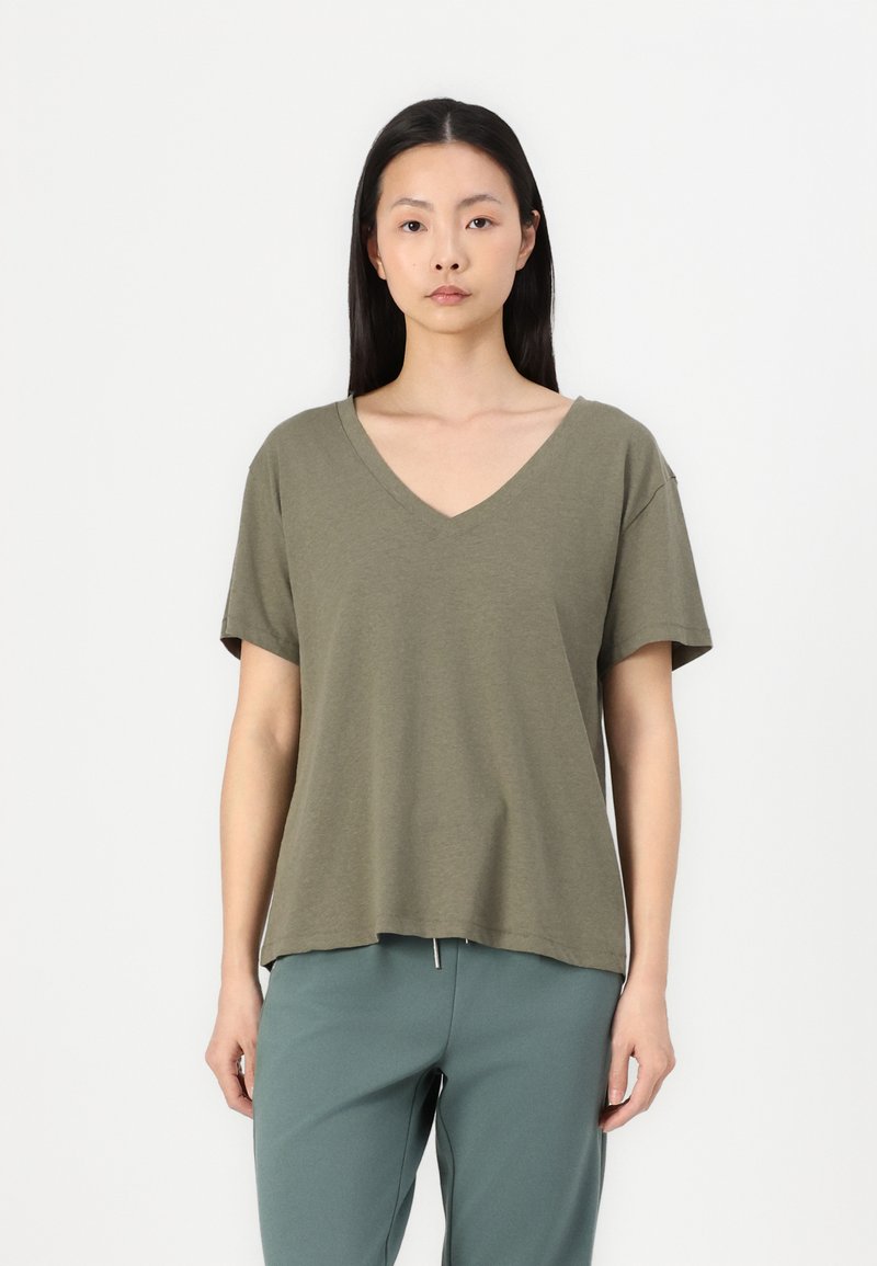 Olive green V-neck t-shirt made of soft fabric with short sleeves and a relaxed fit, paired with light blue green pants.
