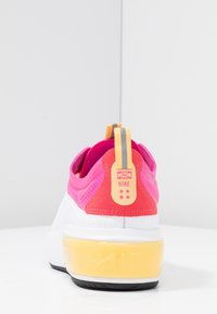 Nike sneaker with a pink upper and white midsole. Features a heel tab with a yellow accent and a transparent yellow air cushion.