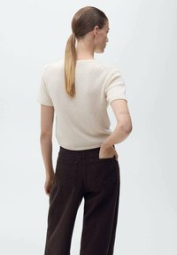 Kortärmad, ljusbeige stickad topp med en avslappnad passform, i kombination med mörkbruna vida byxor. Slät yta, minimalistisk design, inga mönster.