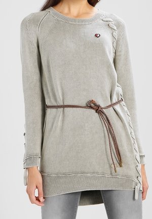 Pull en maille gris clair à manches longues, détails lacés sur les côtés, petit emblème en forme de cœur sur la poitrine, et ceinture tressée marron nouée à la taille.