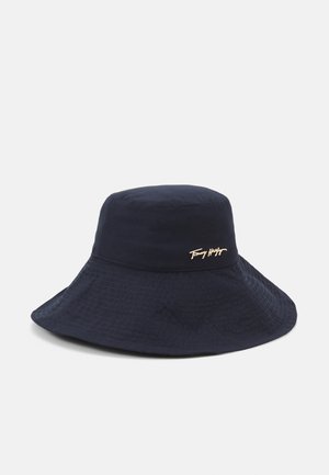 Granatowy kapelusz typu bucket z szerokim rondem, z przeszyciami i małym złotym logo w stylu pisma na przedniej stronie.