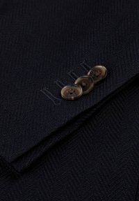 Tela de blazer azul marino con un patrón de espiga. Cuenta con tres botones en tono beige con hilos oscuros, costuras en contraste y un detalle de solapa plegada.