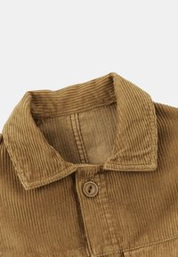 Gros plan du col d'une veste en velours côtelé marron avec un bouton visible et une texture de tissu côtelé vertical.