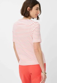 Korte mouwen, gestreepte t-shirt in wit en koraal, met een ronde halslijn en een iets relaxte pasvorm, gestoken in koraalkleurige broeken.