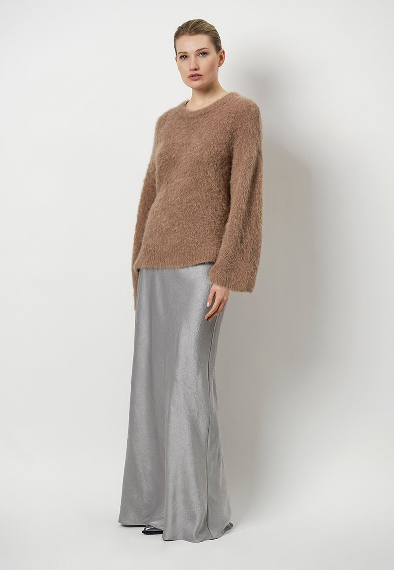 Bruine flaauwtrui met lange mouwen, gecombineerd met een vloeiende zilveren satijnen rok met een subtiele textuur. Eenvoudige, elegante silhouet.