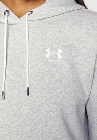 Ljusgrå hoodie i mjukt material, med en frontficka och snoddar med metallspetsar. Broderad Under Armour-logotyp på bröstet.