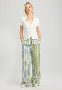 White ribbed short-sleeve cardigan with buttons paired with green, blue, and yellow striped wide-leg pants with a drawstring waist.