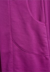 Gros plan d’un vêtement violet montrant une couture détaillée et une couture de poche courbe sur un tissu lisse.
