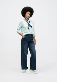 Απαλή μπλε ριγέ μπλούζα με τρία τέταρτα μανίκια, συνδυασμένη με ψηλόμεσα σκούρα τζιν παντελόνια με φαρδιά κόψιμο και λευκά αθλητικά παπούτσια. Διακοσμημένη με ένα μοτίβο μαντήλι.