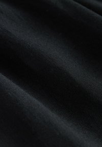 Sort stof med en glat tekstur, der har subtile vævede mønstre, som skaber bløde folder og skygger over overfladen.