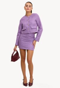 Veste cropped en tweed violet avec des boutons dorés et des poches avant, assortie à une jupe mini ajustée et un sac à main texturé bordeaux.