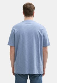 Jasnoniebieska koszulka z krótkim rękawem o luźnym kroju, okrągłym dekolcie i lekko teksturowanej tkaninie, widoczna z tyłu.