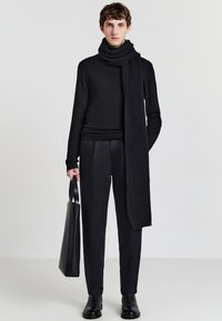 Maglione nero in lana e sciarpa a costine, abbinati a pantaloni neri su misura. Una borsa in pelle liscia e stivaletti alla caviglia completano l'outfit.
