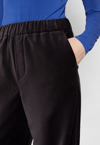 Pantalons en velours noir avec une taille élastique et des poches latérales, associés à un haut à manches longues bleu. Gros plan sur le tissu et la coupe.