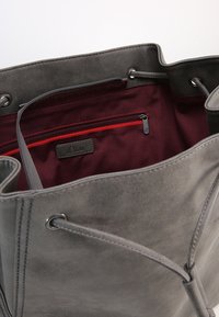 Grå ruskinds tote bag med en burgunderrød stofindvendig. Har en lynlåslomme og metalhardware detaljer. Åben top med snorelukning.