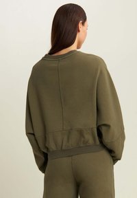 Sudadera corta de algodón suave en verde oliva con un ajuste amplio, puños y bajo acanalados. Presenta un detalle de costura central en la parte trasera.