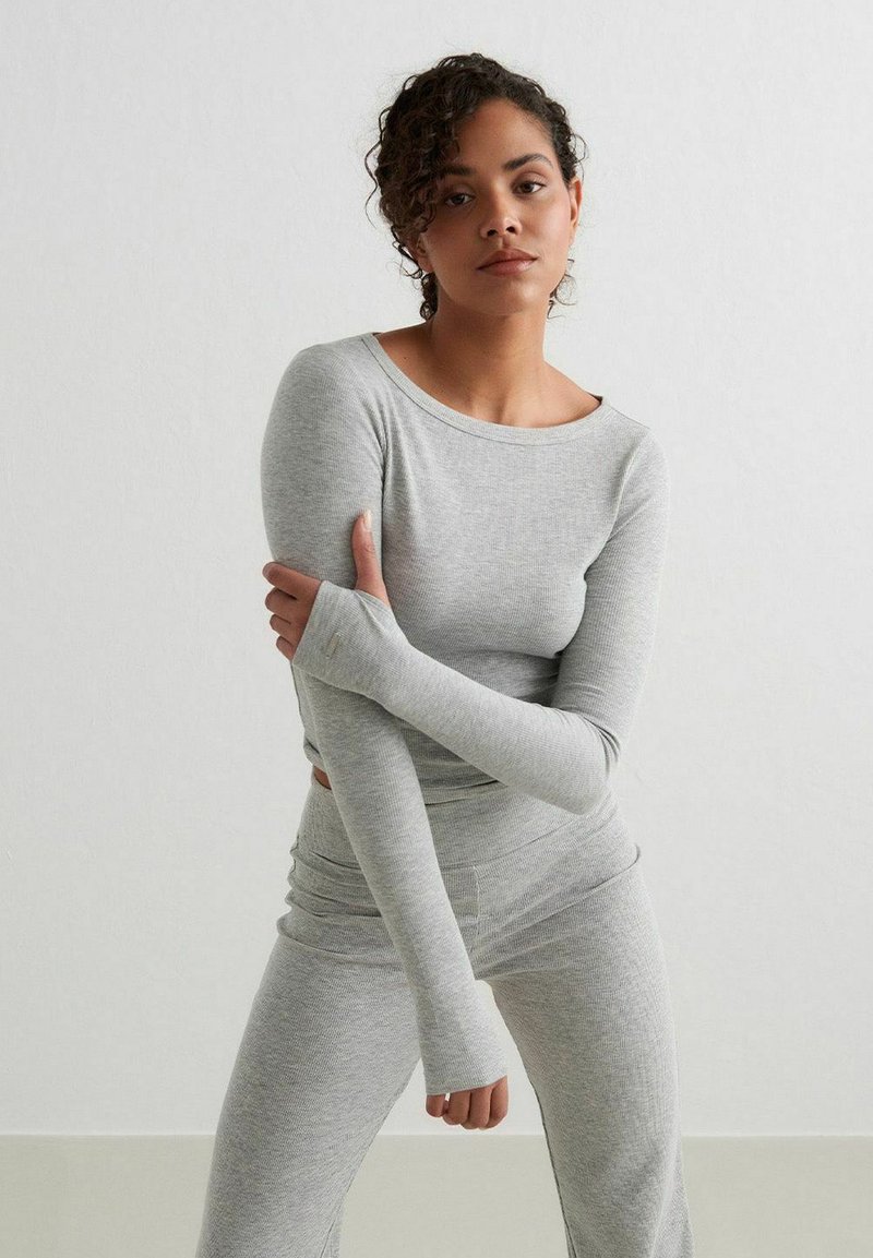Top grigio a maniche lunghe e leggings abbinati realizzati in tessuto a coste, con aperture per il pollice e scollatura rotonda, su uno sfondo semplice.