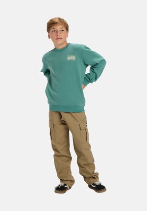 Green sweatshirt with crew neck and logo on chest, paired with khaki cargo pants featuring side pockets and black sneakers.