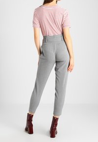 Grijze, taps toelopende broeken met een hoge taille, gecombineerd met een roze en witte gestreepte shirt met korte mouwen en glanzende bordeauxrode enkellaarsjes.