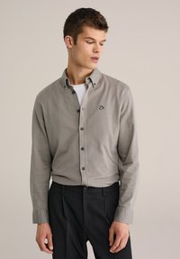 Camisa gris abotonada con un patr�ón texturizado, botones negros y un pequeño gráfico bordado. Se lleva sobre una camiseta blanca de cuello redondo.