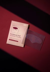 Une compresse pour le front en matériau gel transparent, entourée d'un emballage rose et blanc avec un design graphique mettant en avant la technologie hexapeptide.
