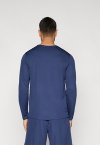 Μπλε σκούρο μακρυμάνικο πουκάμισο από αναπνεύσιμο ύφασμα, με απλό στρογγυλό λαιμόκοψη και ραφές κατά μήκος του τελειώματος και των μανσετών.