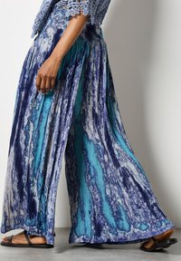 Pantaloni a gamba larga con un design fluido in blu e turchese con un motivo tie-dye, realizzati in un tessuto leggero e testurizzato.