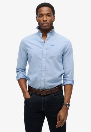 Camisa de botones azul claro hecha de algodón, con cuello, mangas largas enrolladas en los puños y un pequeño bolsillo en el pecho con logotipo.
