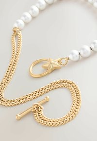 Zlatý náhrdelník s bielymi perlami. Obsahuje klip vo tvare hviezdy a zapínanie na korálky. Textúrované články a hladké, lesklé korálky.