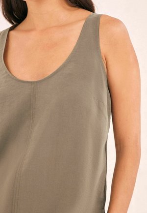 Vrouw in een mouwloze olijfgroen top met een ronde hals en verticale naaddetails aan de voorkant.