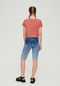 Katoenen t-shirt in roze kleur, gecombineerd met lichtblauwe denim shorts met een middelhoge taille, een lichte wasbeurt, gescheurde zoom en achterzakken. Zwarte sandalen gedragen.