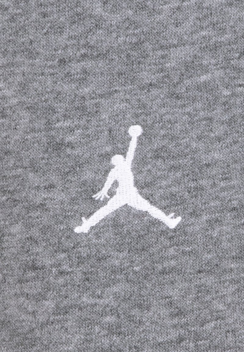 Tissu gris avec un logo Jumpman brodé en blanc, représentant une figure en plein saut tenant un ballon de basket. Texture douce, design athlétique.