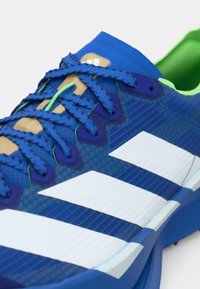 Μπλε αθλητικό παπούτσι με επάνω μέρος από δίχτυ, λευκές ρίγες, πράσινες λεπτομέρειες και κορδόνια με υφή. Διαθέτει επενδυμένη γλώσσα και μαλακή σόλα.