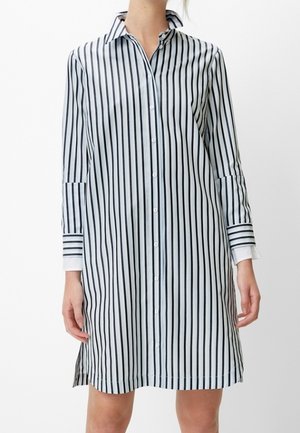 Woman wearing a long-sleeve, knee-length white dress with vertical black stripes and button-down front.
