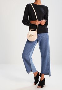 Sudadera negra, jeans anchos azules con dobladillos sin terminar, tacones negros destalonados y un pequeño bolso cruzado color crema con cierre de solapa y detalles en dorado.