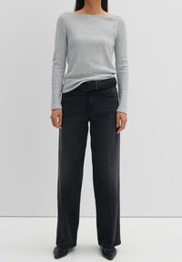 Ljusgrå långärmad topp med båturringning, ihop med högmidjade, vida svarta jeans och ett strukturerat svart bälte.