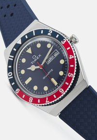 Timex quartz watch with a stainless steel case, navy silicone strap, red and blue bezel, and yellow hour markers. Date display at 3 o'clock.