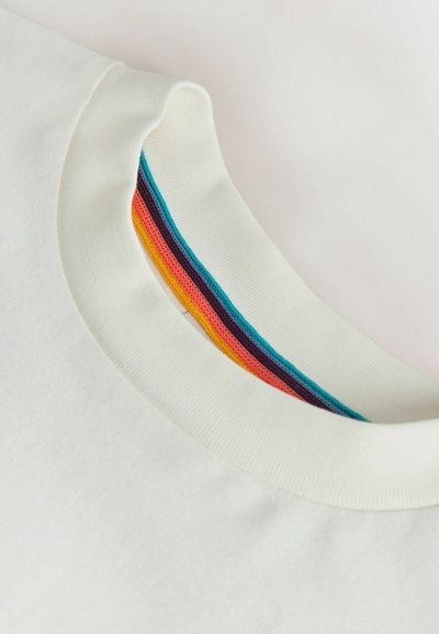 Gros plan sur le col d'un t-shirt blanc à col ras du cou, avec une bordure intérieure en tissu aux rayures bleu sarcelle, violet, rouge et orange.