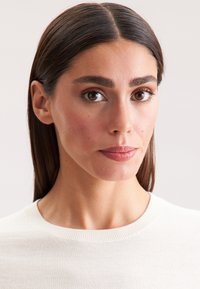 Maglione bianco a maglia con colletto a coste, indossato da una persona con capelli lunghi e lisci. Pelle liscia con trucco naturale e colore labbra neutro.