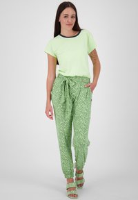 Tricou scurt verde deschis cu guler bleumarin, asortat cu pantaloni jogger verzi cu model și sandale ondulate corespunzătoare.