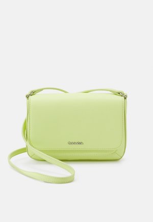 Světlounce zelená crossbody kabelka Calvin Klein s klopou a nastavitelným popruhem na bílém pozadí.
