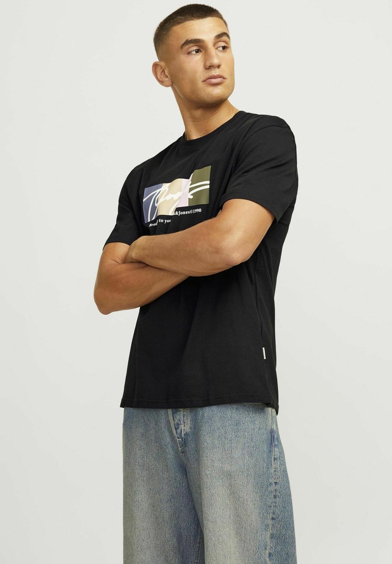 Camiseta de algodón negra con un gráfico colorido en el frente, escote redondo y mangas cortas; combinada con unos pantalones vaqueros de mezclilla azul claro.