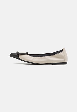 Ballerine avec un dessus crème, un capuchon noir et un accent texturé. Le design est minimaliste avec une silhouette basse.