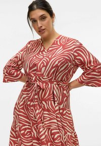 Robe à motif rouge et crème avec un décolleté en V, des manches trois-quarts, une taille ceinturée et une jupe à étages. Tissu texturé avec des rayures ondulées.